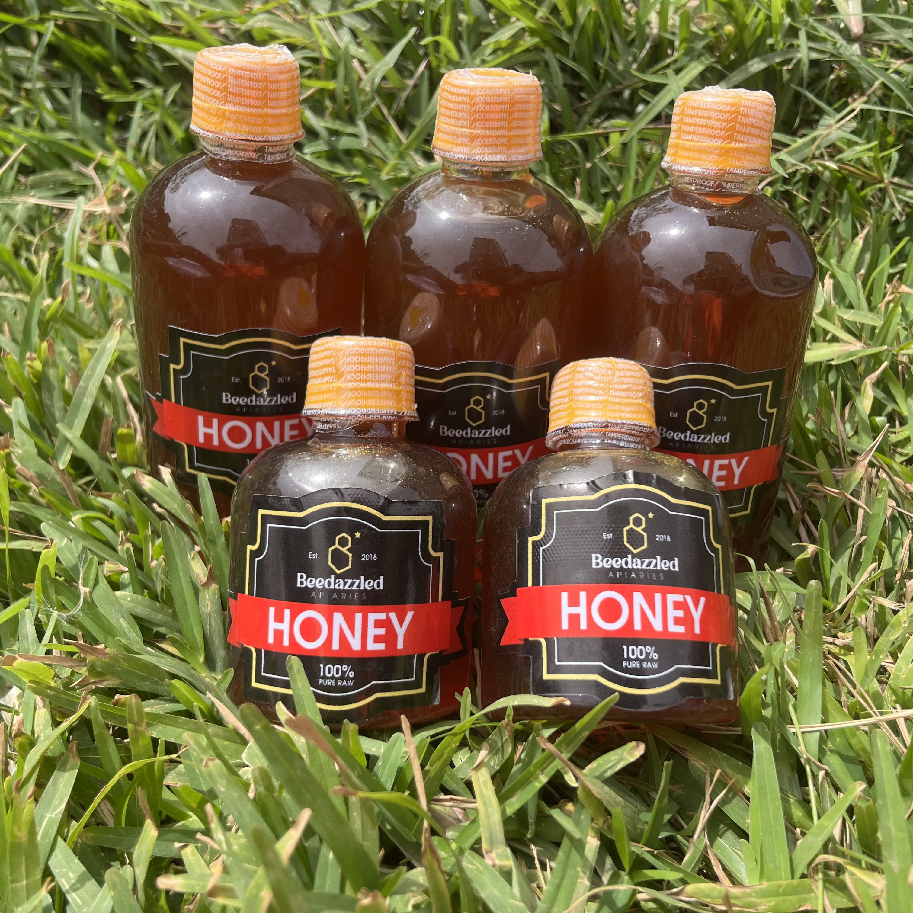 Beedazzled labelled honey bottles standing in grass